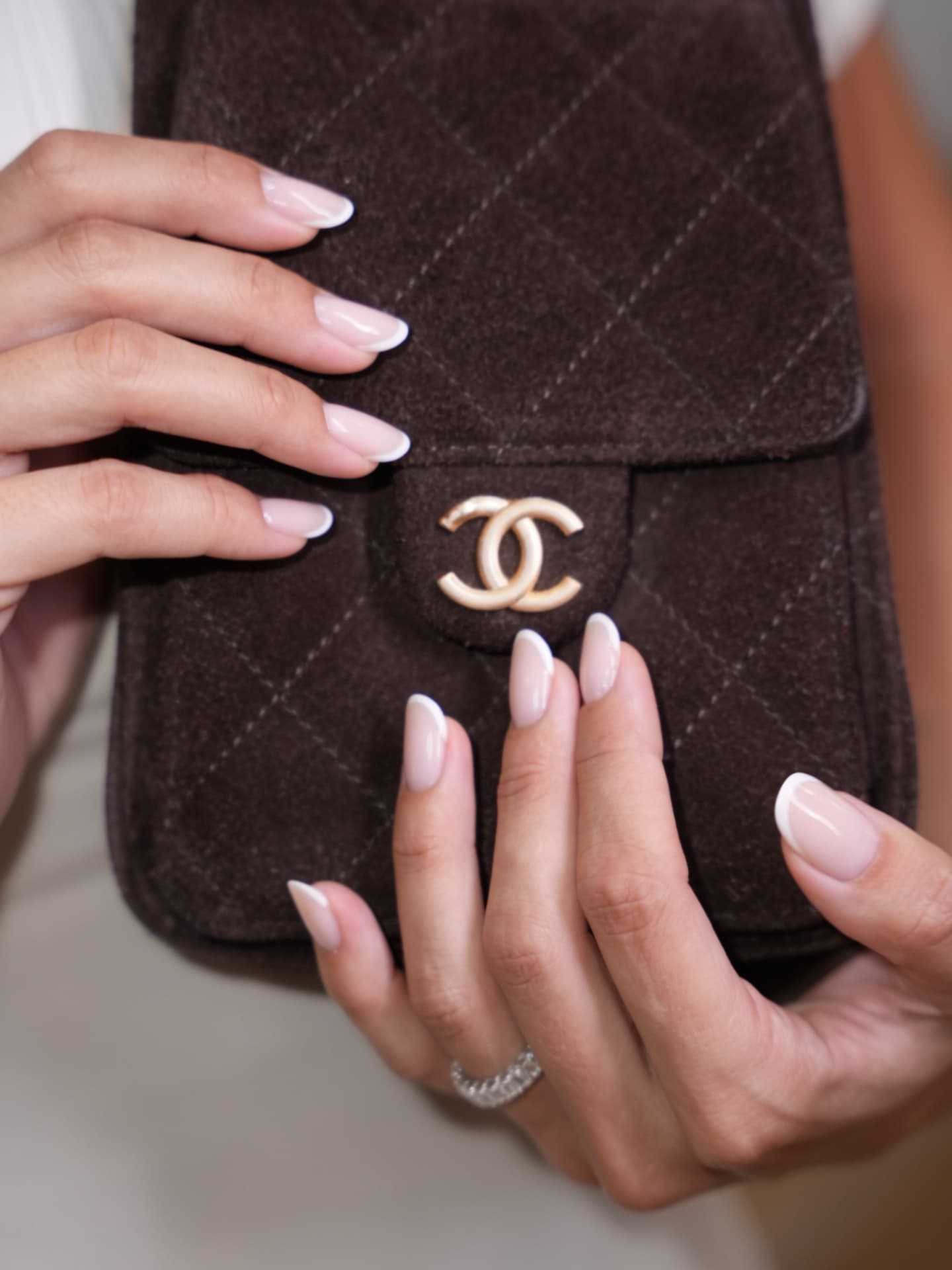 French-manicured nails resting beside a quilted brown handbag
