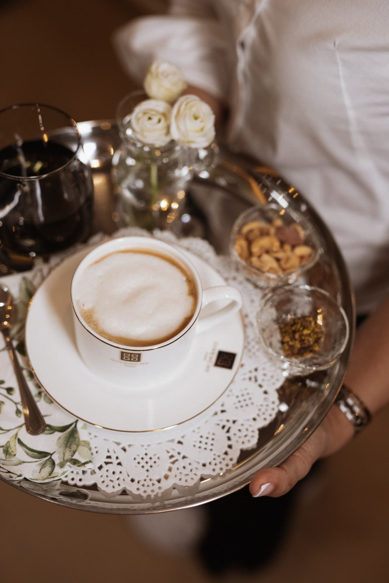 A silver tray with coffee, water, nuts and white ranunculus brought to a client
