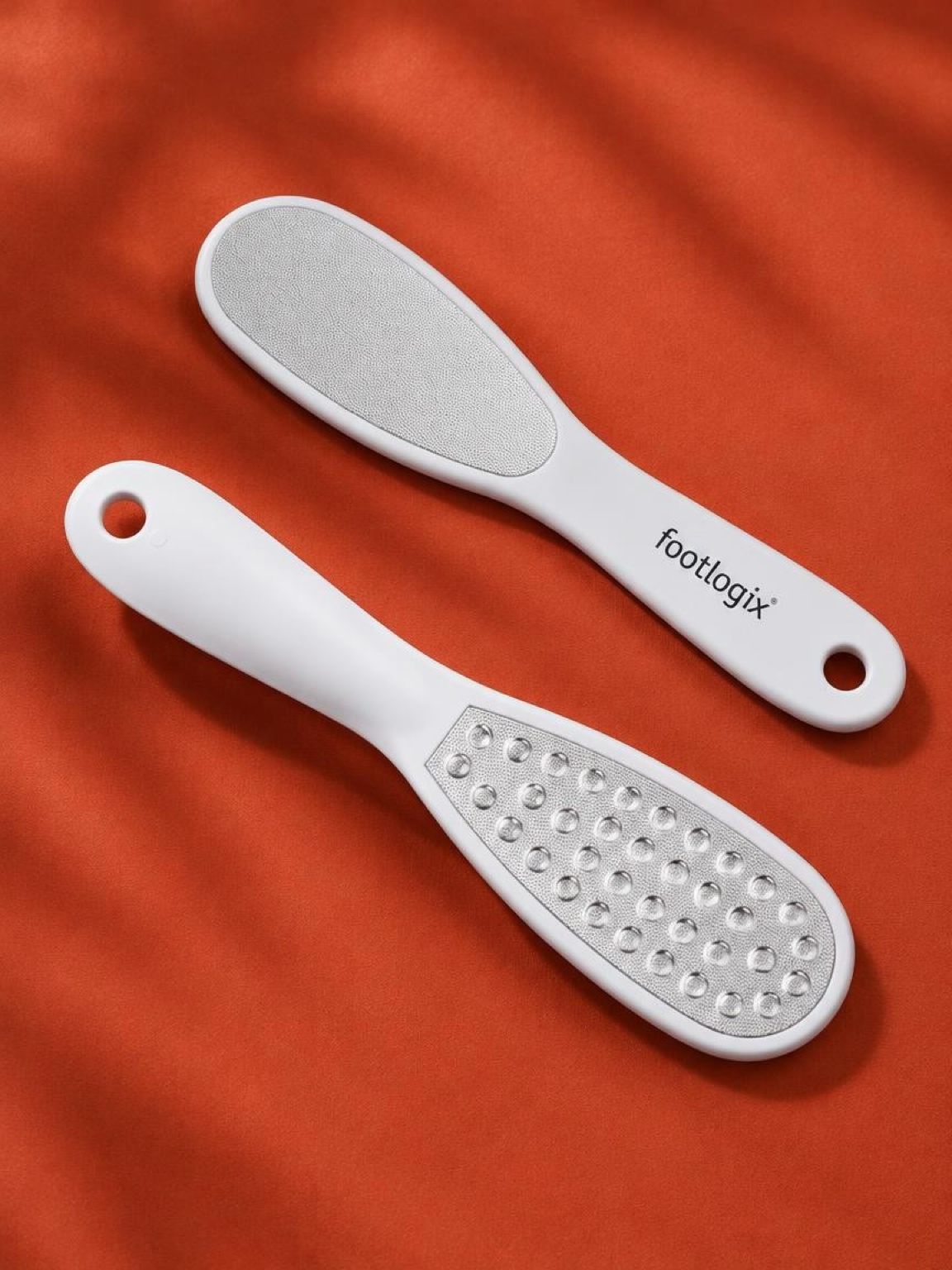 Footlogix double-sided metal foot file resting on terracotta fabric