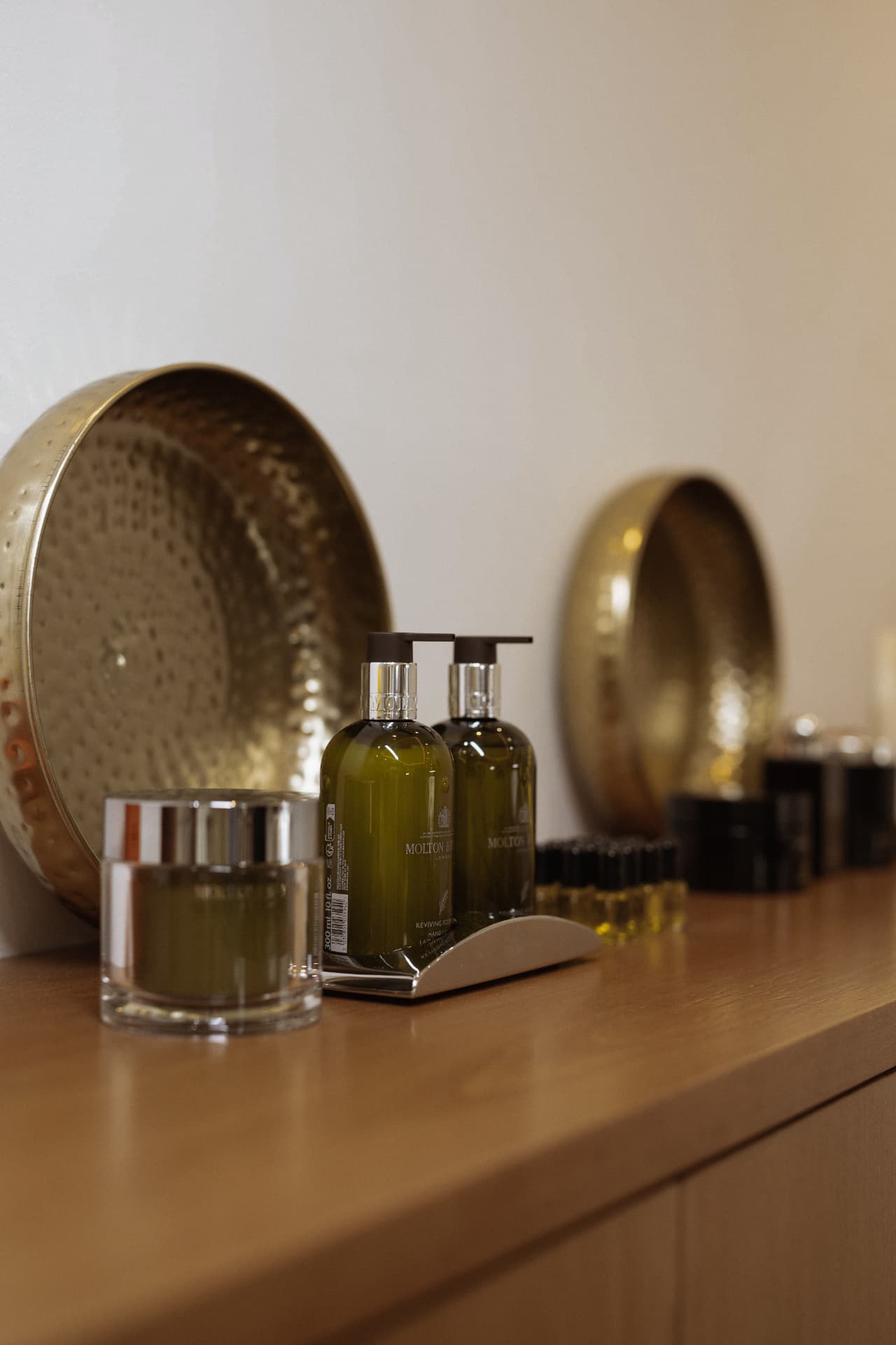 Hand-care bottles and hammered brass dishes arranged on a wooden shelf