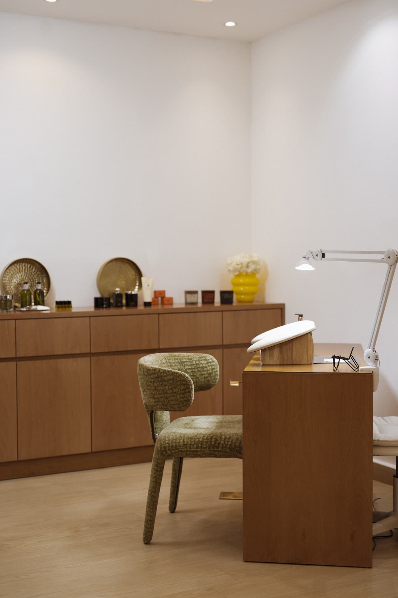 A manicure desk with armrest and lamp beside a moss-green armchair